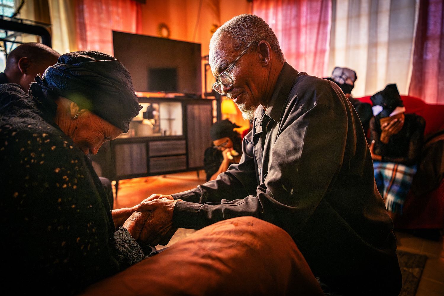 Elderly couple holding hands warmly in a cozy living room, sharing an intimate moment together.