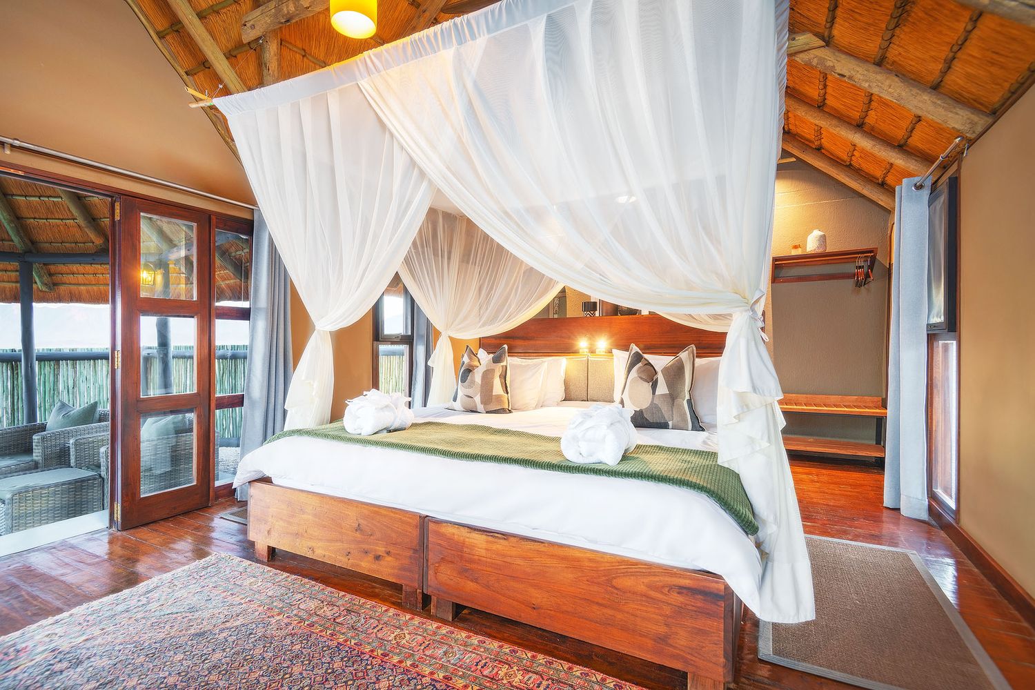 Luxury safari bedroom with white canopy four-poster bed, wooden floors, and private deck access.