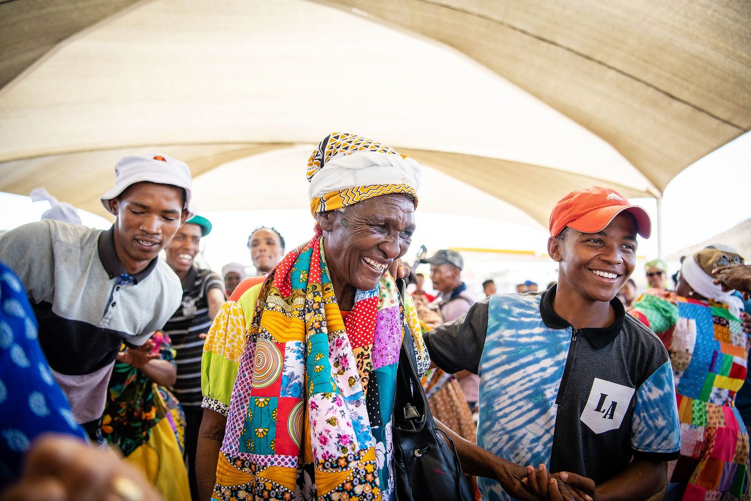 Joyful African women in colorful traditional attire smiling and celebrating together at an outdoor community gathering.