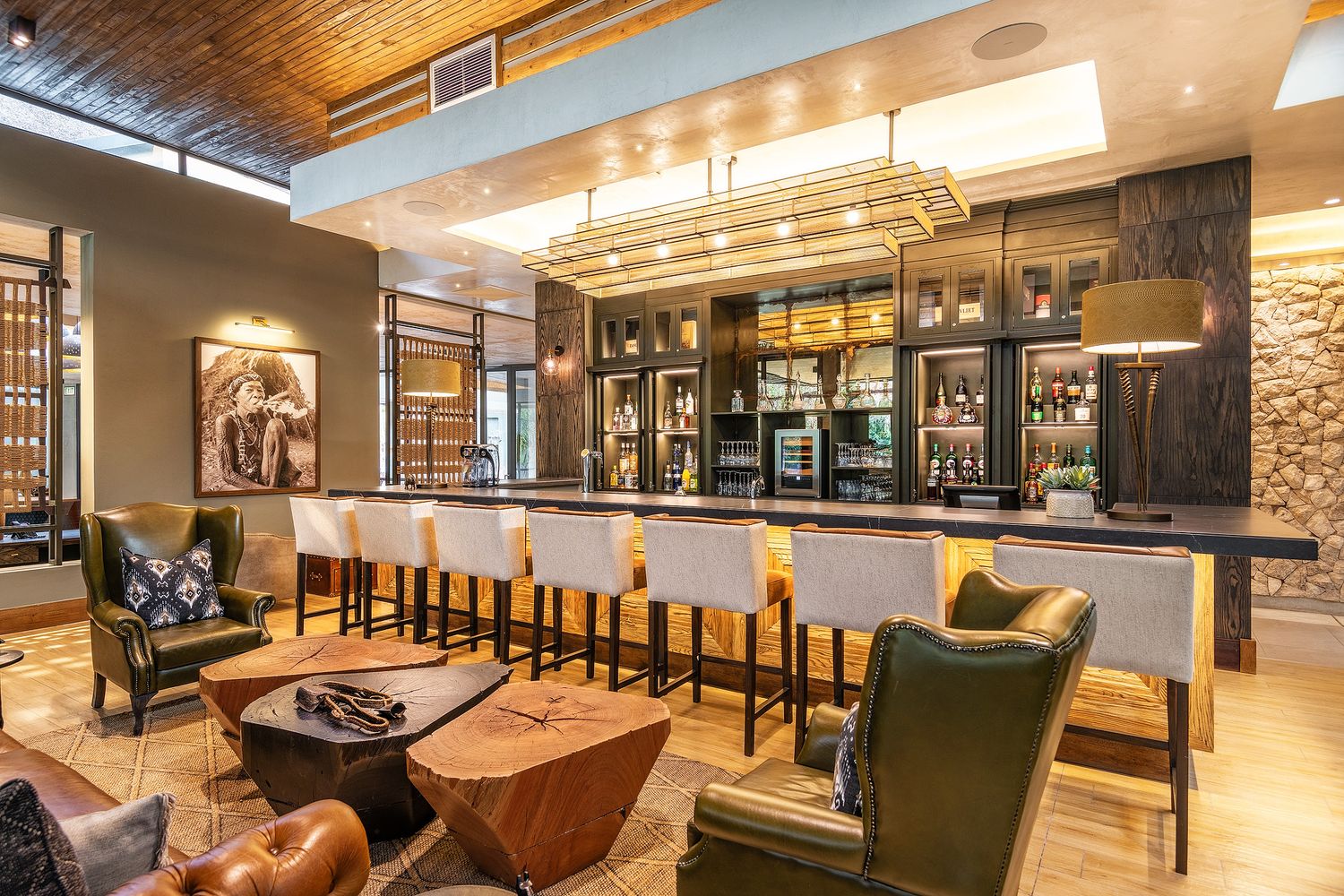 Elegant safari lodge bar with high stools, warm lighting, and plush leather seating in a sophisticated lounge setting.