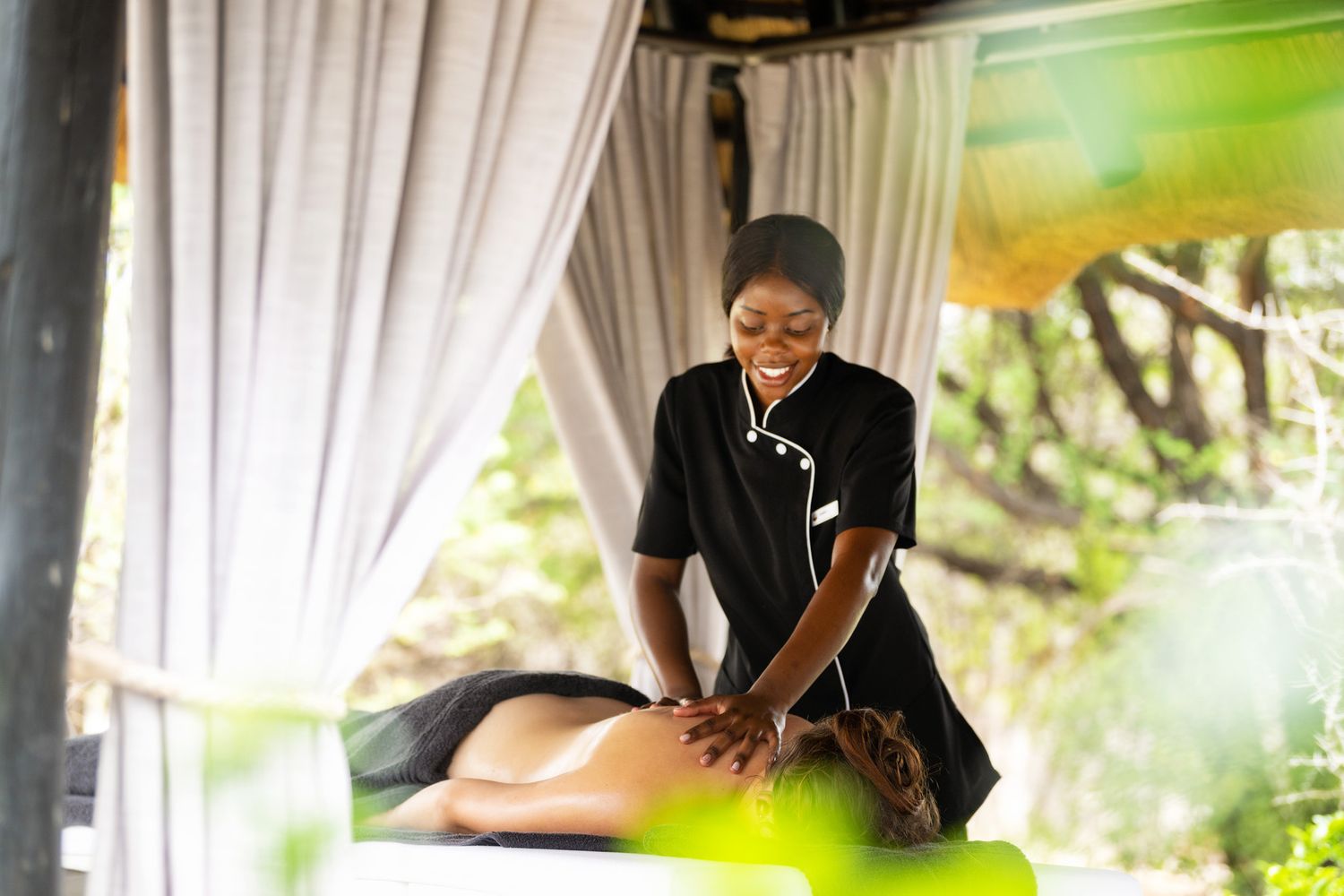 A spa therapist performs an outdoor massage under a white canopy surrounded by lush tropical greenery.
