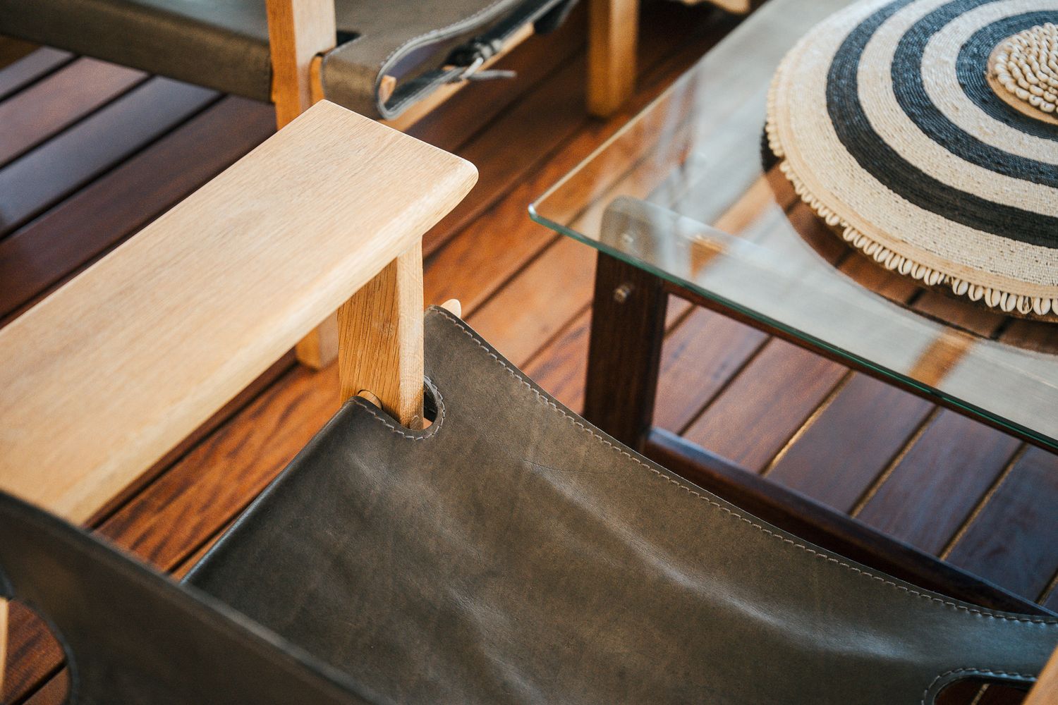 Close-up of wooden deck furniture featuring a leather chair, light wood bench, glass table, and striped woven placemat.