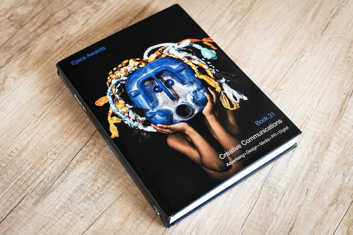 Book titled Creative Communications on a wooden surface featuring vibrant blue and gold artistic cover design.