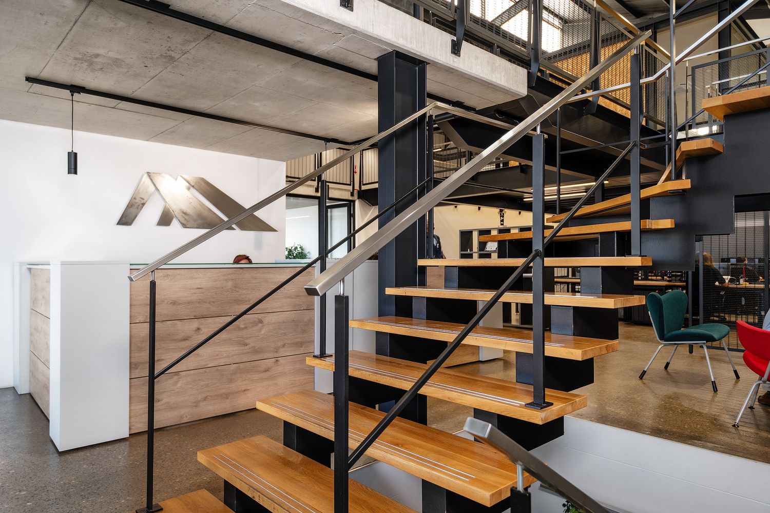 Modern industrial office space featuring black steel staircase with wooden steps, concrete ceiling, and open workspace area.