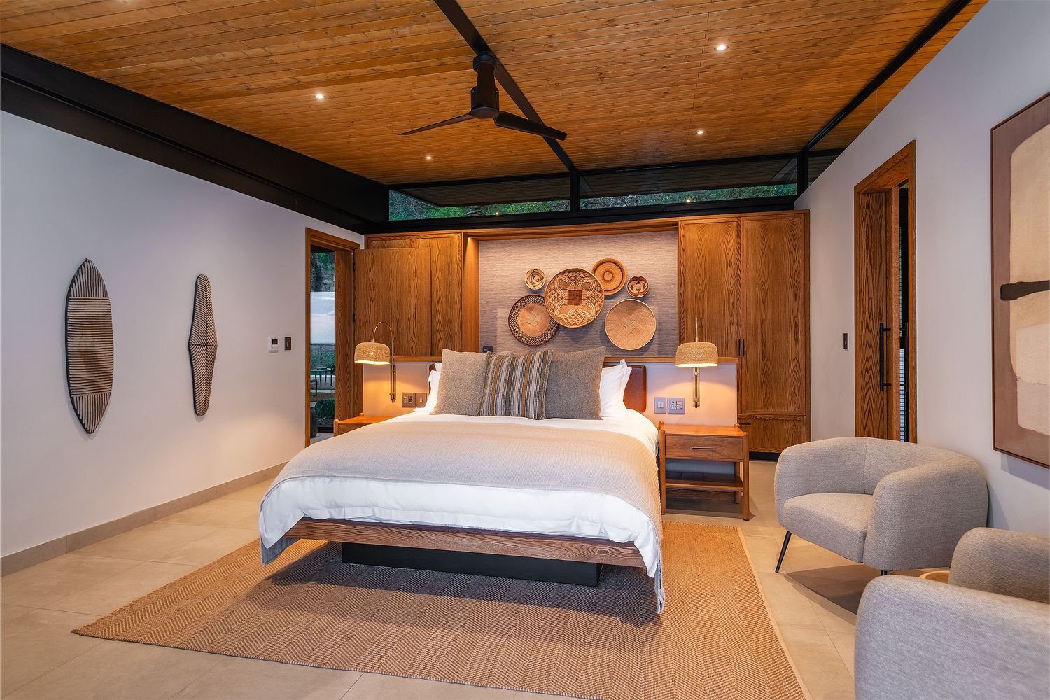 Luxury safari bedroom with wooden ceiling, decorative wall baskets, king bed, and neutral earth-tone decor.