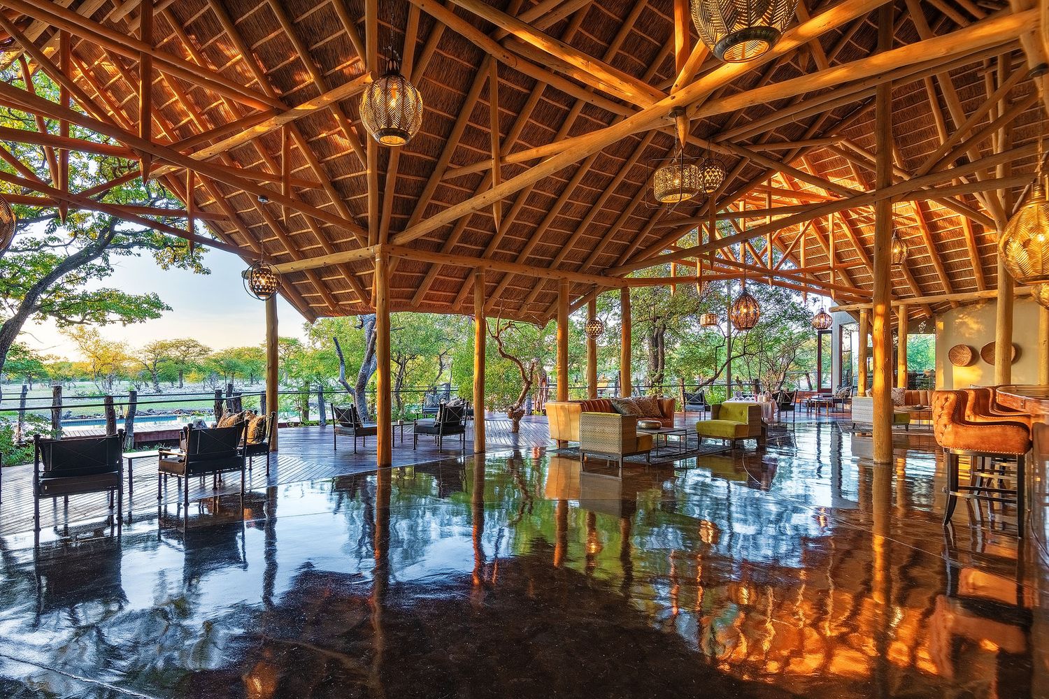 Elegant open-air bamboo pavilion lodge with reflective floors, pendant lights, and lush tropical views at golden hour.
