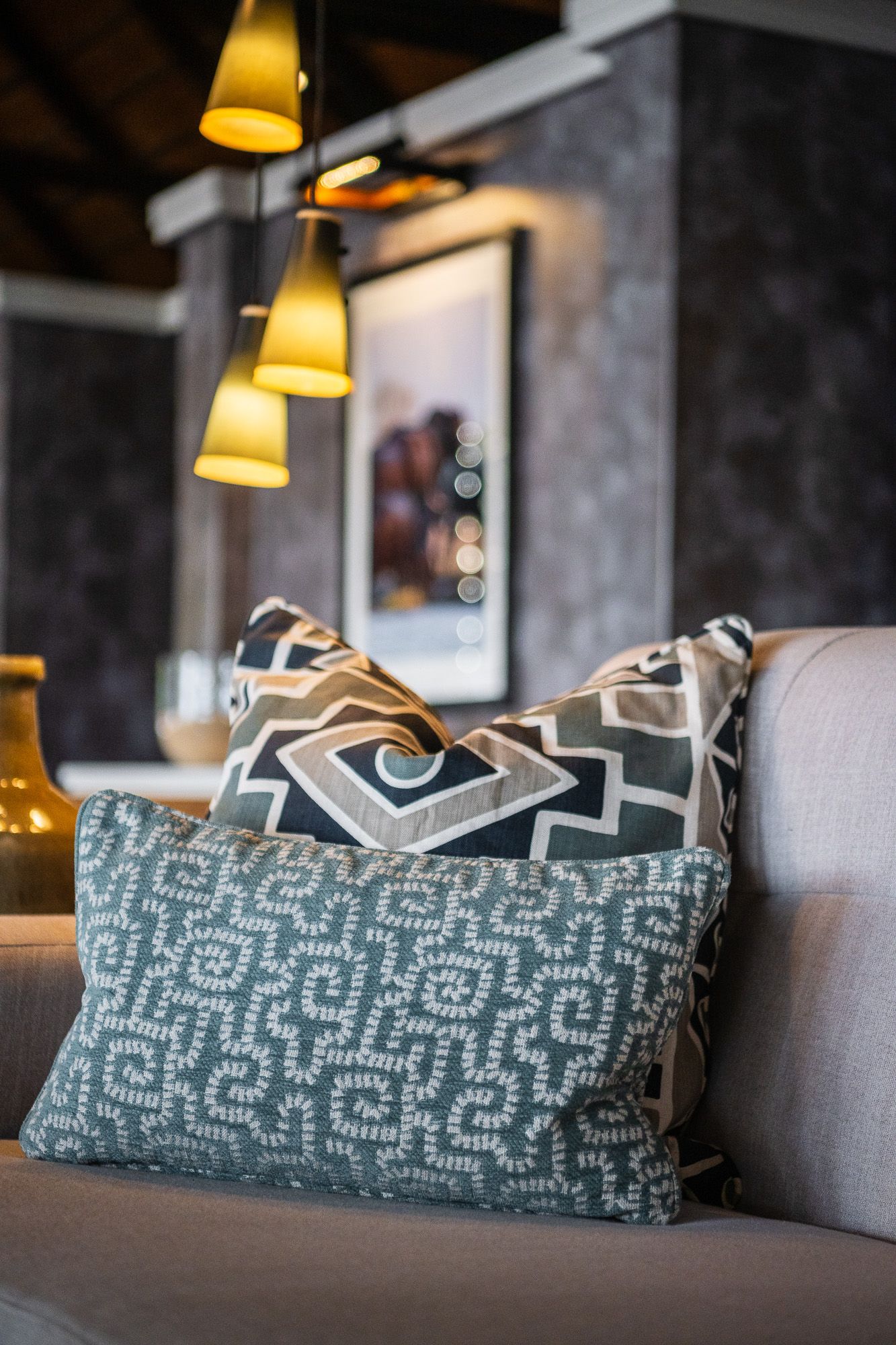 Decorative patterned throw pillows on a beige sofa with pendant lights and framed artwork in a stylish living room.