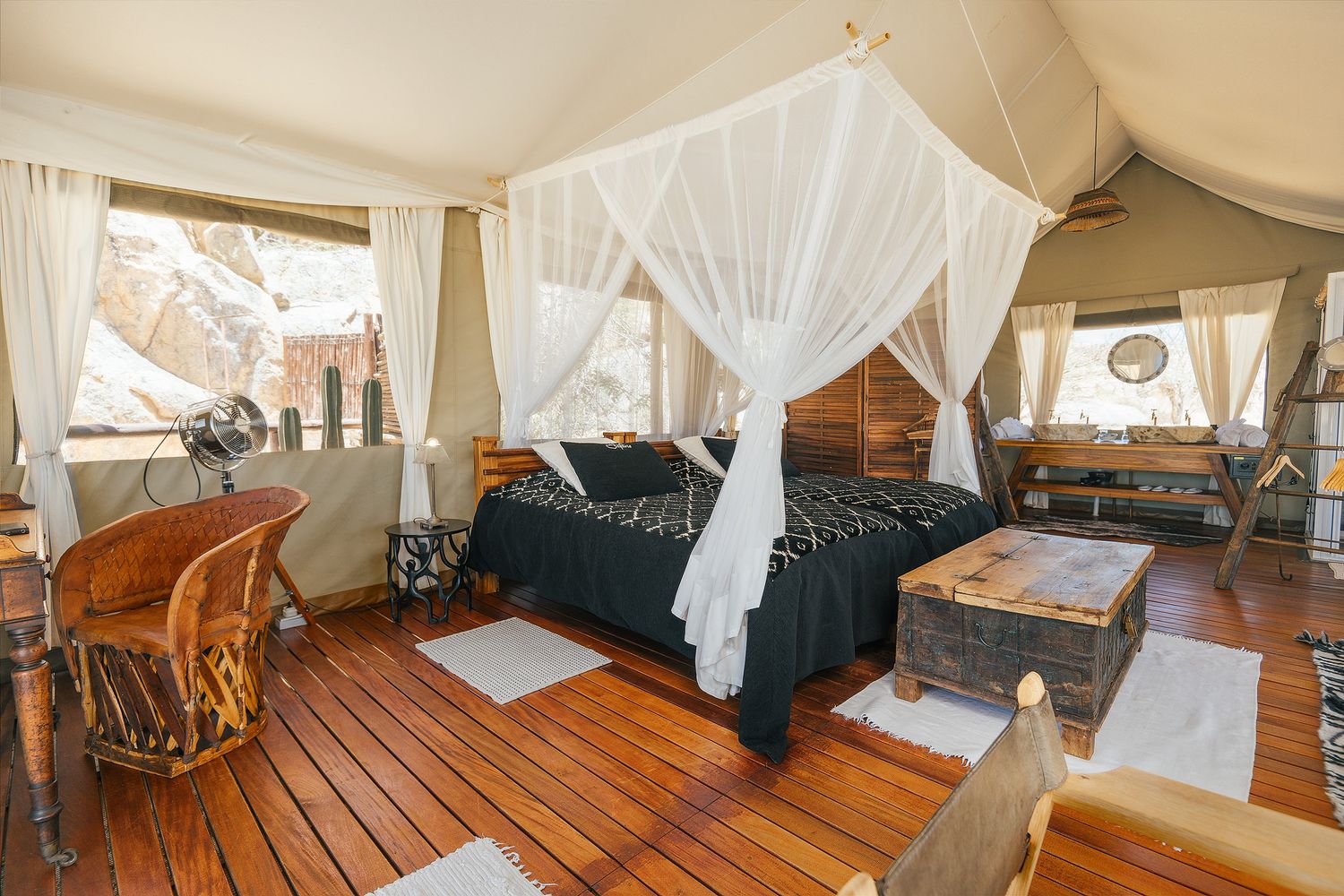 Luxury safari tent bedroom with canopy bed, wooden deck floor, and natural light streaming through canvas walls.