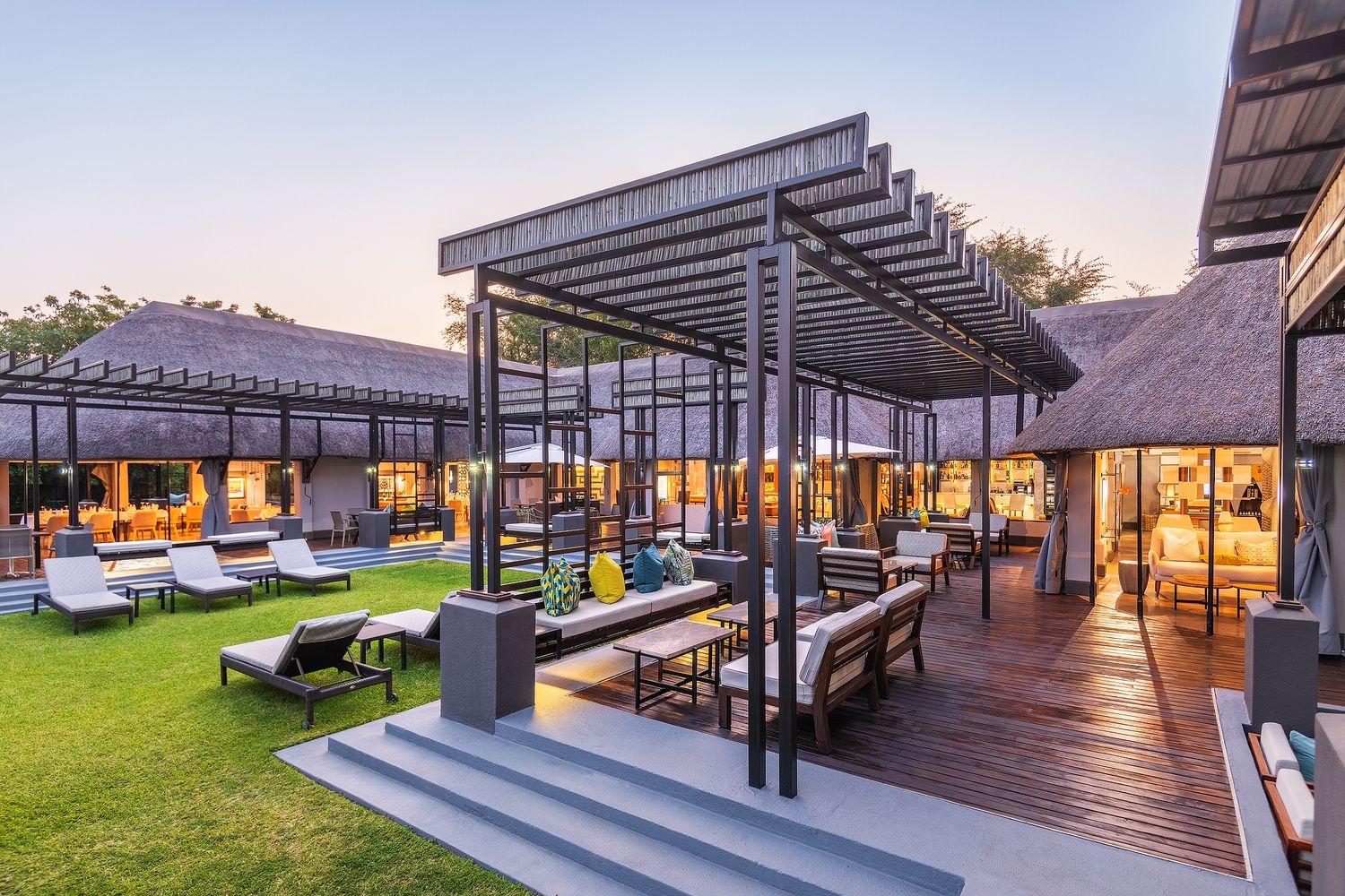 Elegant outdoor resort terrace with pergola, lounge chairs, and lush lawn at dusk.