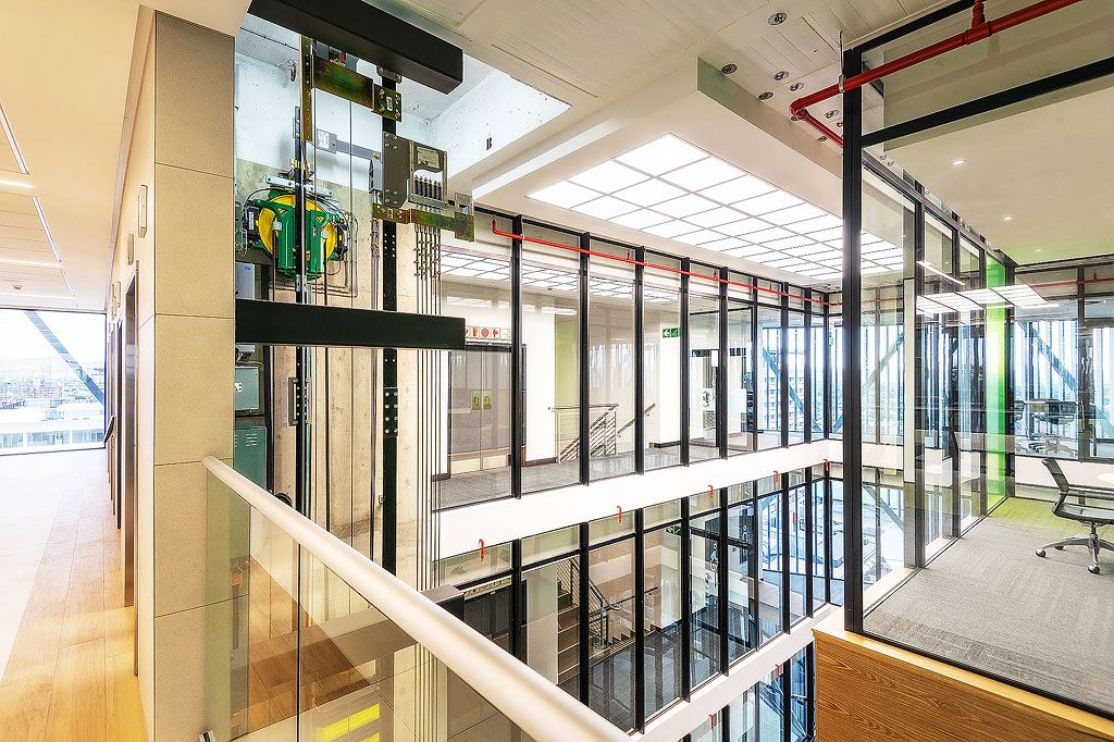 Contemporary open-plan office interior featuring glass partitions, mezzanine level, and modern industrial design elements.