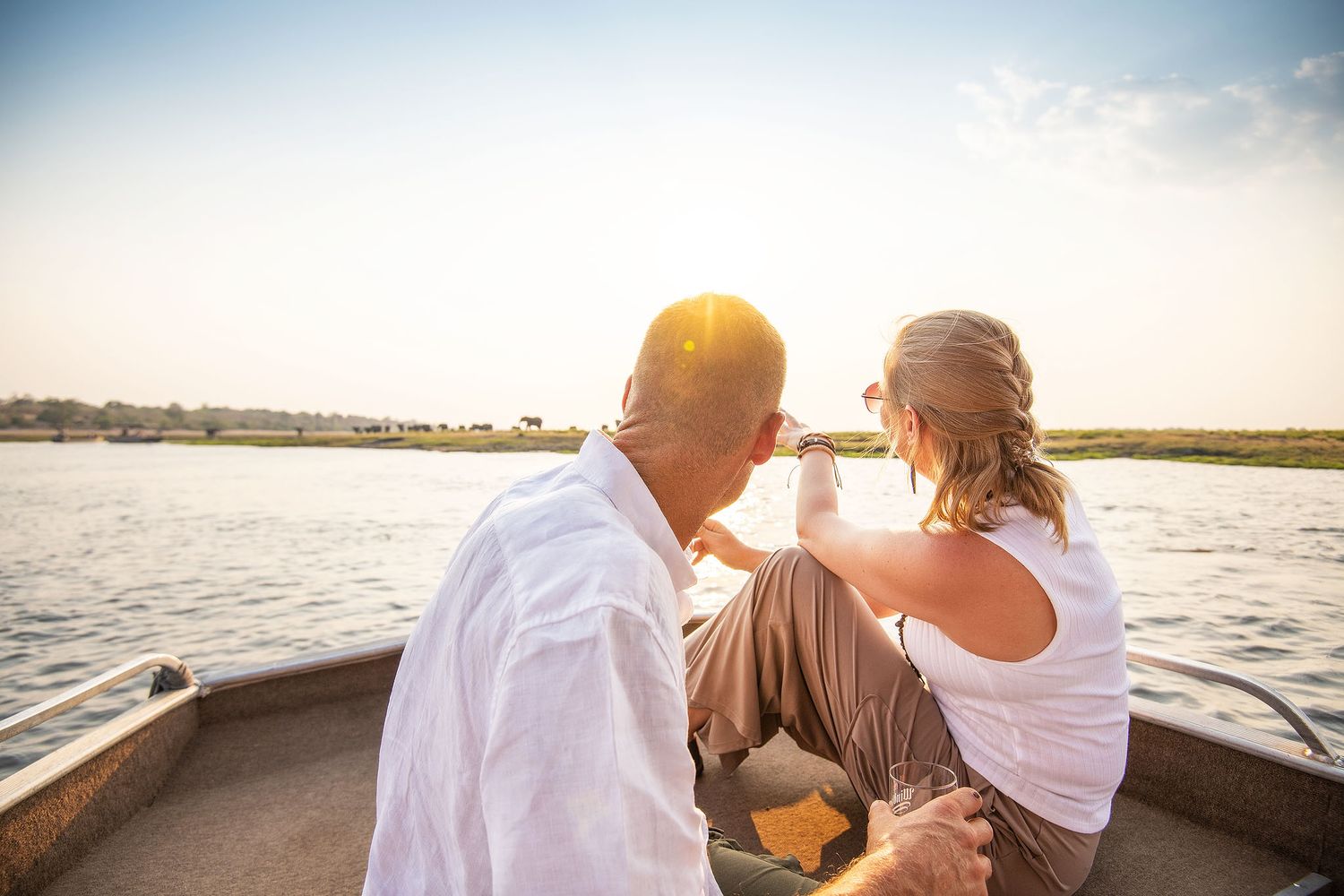 Couple toasting with drinks on a boat during a golden sunset river cruise in Africa.