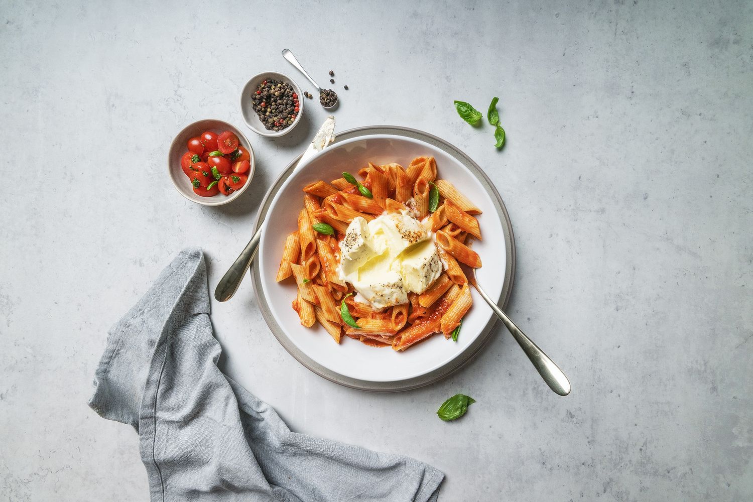 Penne pasta in tomato sauce topped with fresh burrata cheese, served in a white bowl with basil and cherry tomatoes.