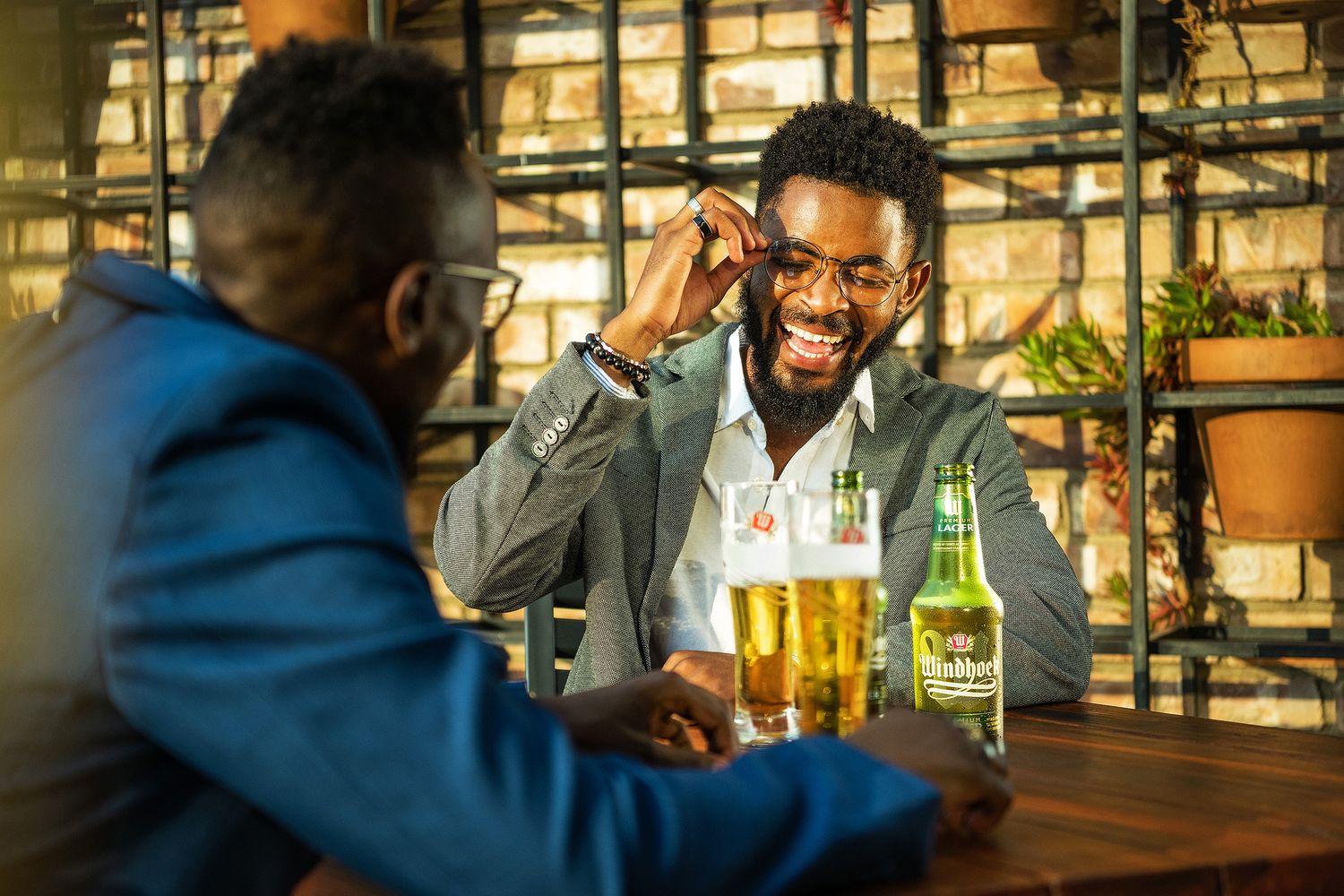 Two men enjoying drinks at a bar, one smiling broadly with glasses of beer and a Heineken bottle on the counter.