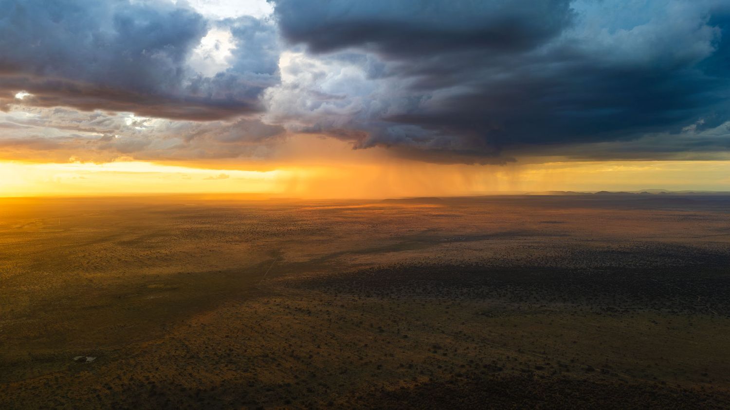 Dramatic aerial sunset over African savanna with storm clouds and rain in the Kalahari Desert, Namibia.