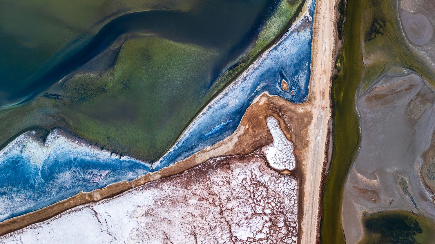 Aerial view of colorful salt flats with blue, green, and white patterns.