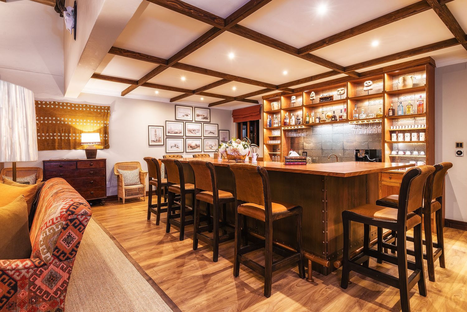 Elegant hotel bar with wooden coffered ceiling, bar stools, and backlit shelves stocked with bottles.
