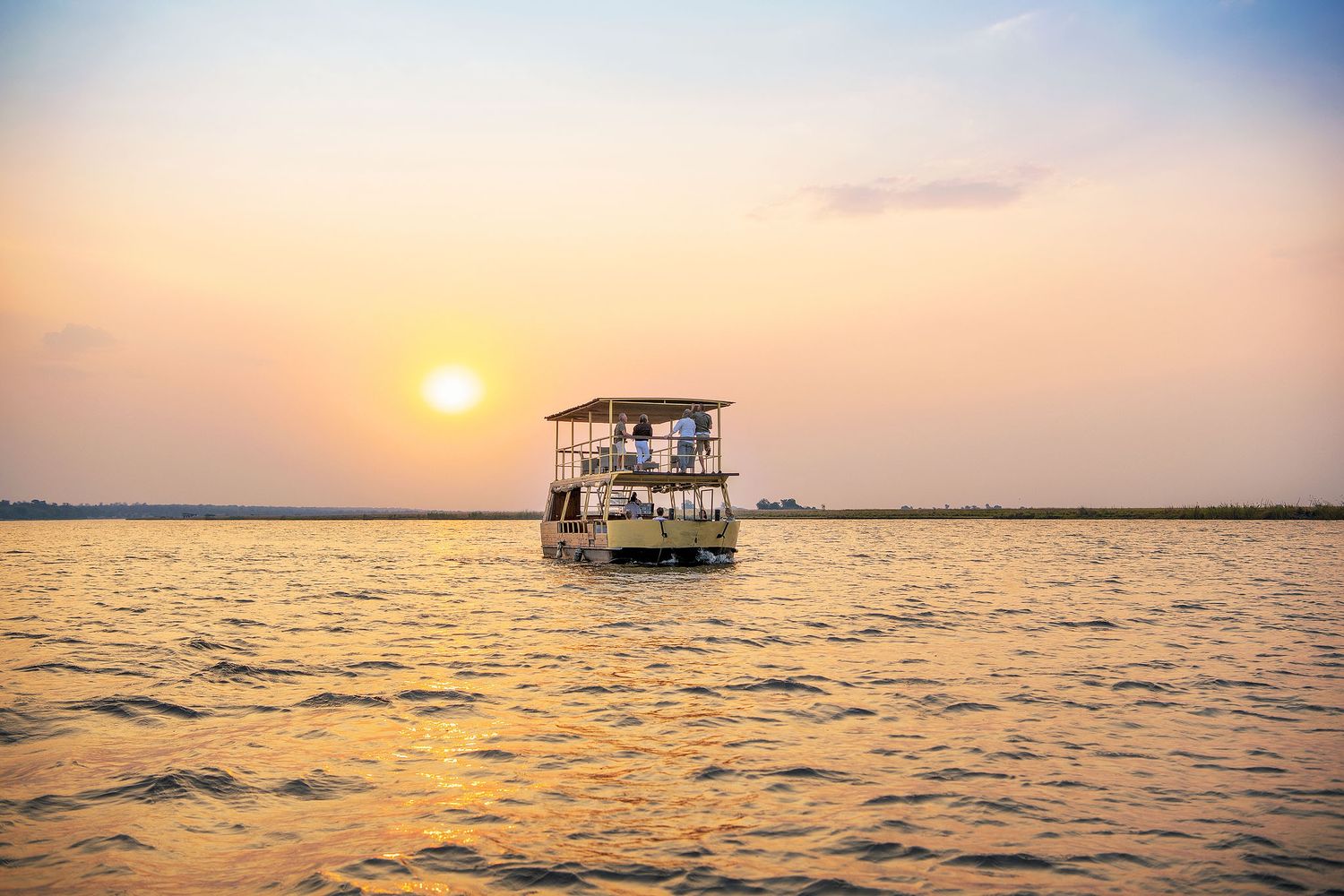 Small safari houseboat cruising on golden waters during stunning African sunset in vast open waterway.