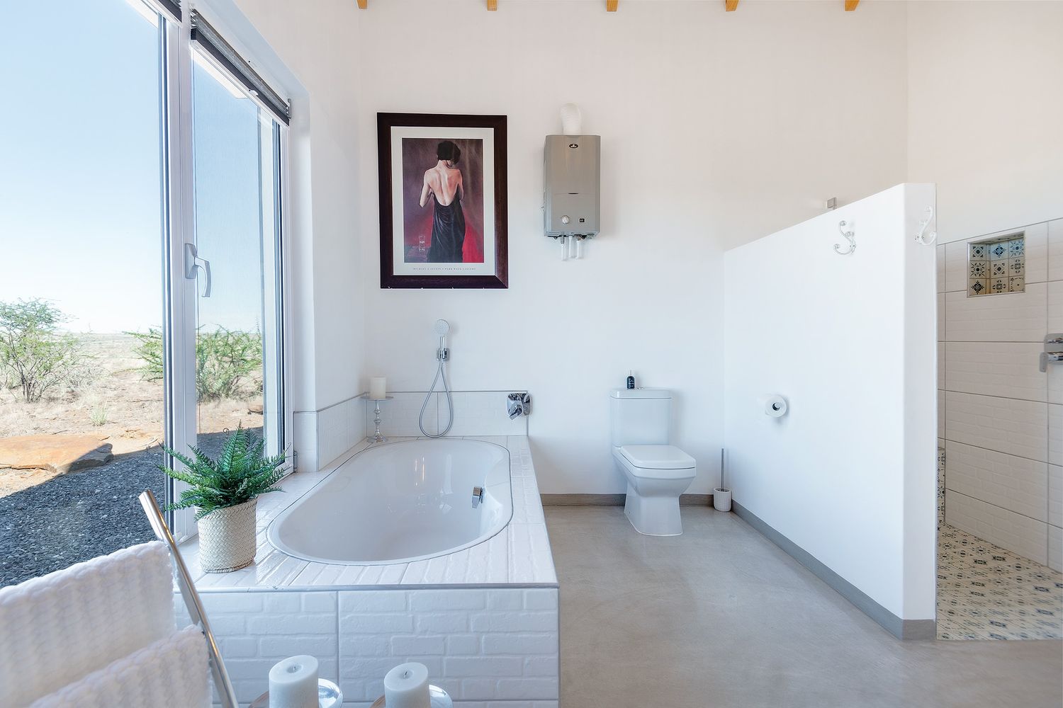 Bright white bathroom with freestanding tub, large window, and scenic Namibian desert views.