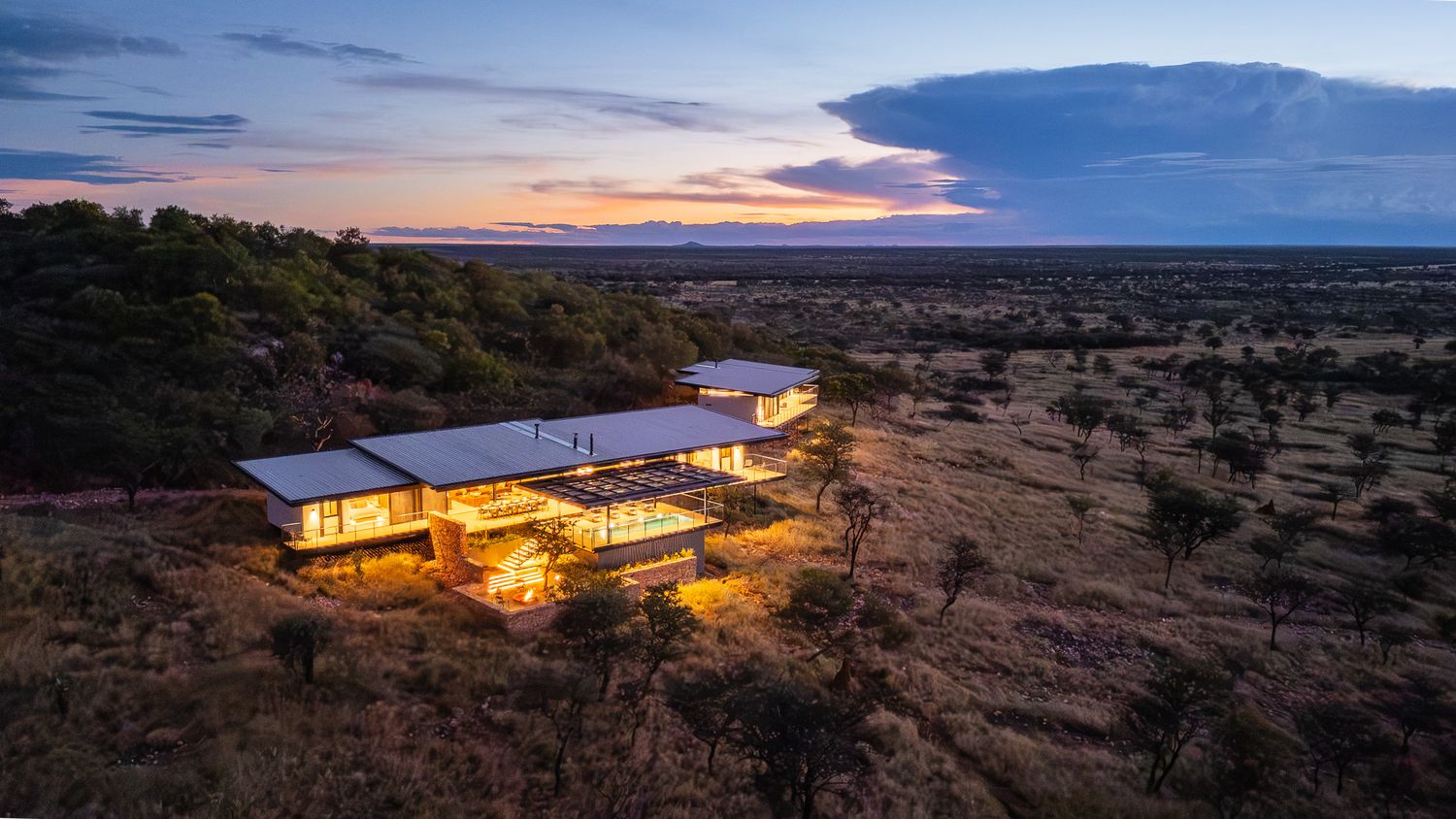 Aerial view of a modern luxury lodge illuminated at twilight surrounded by vast African bushveld.
