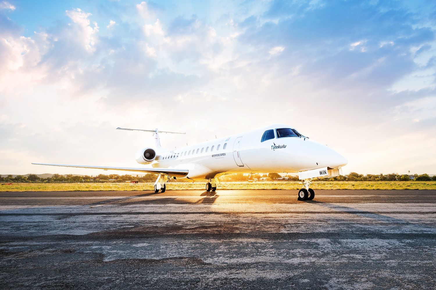 White private jet aircraft parked on runway at sunset with dramatic cloudy sky backdrop.