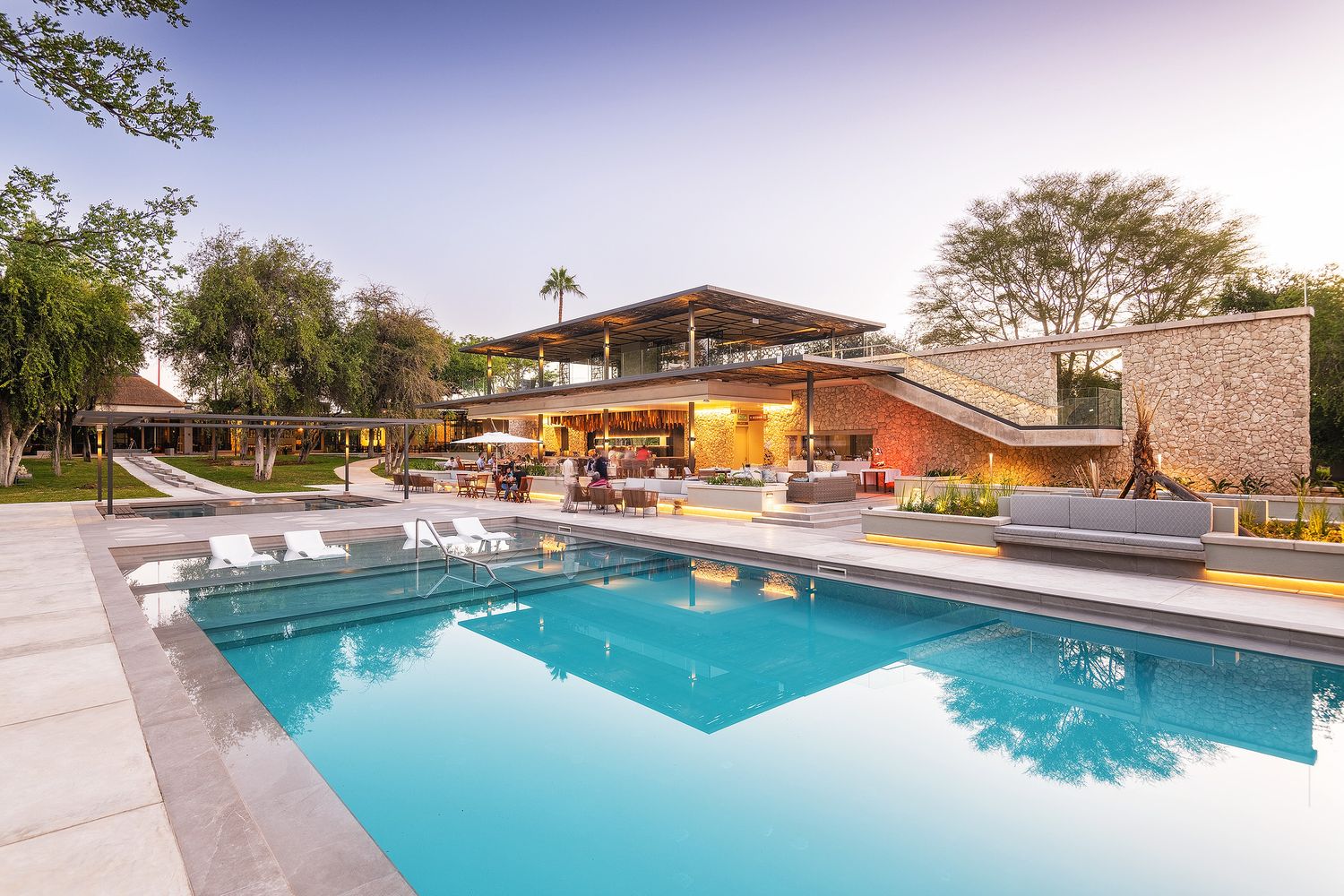 Luxury modern home with large rectangular swimming pool, outdoor lounge area, and illuminated interior at dusk.