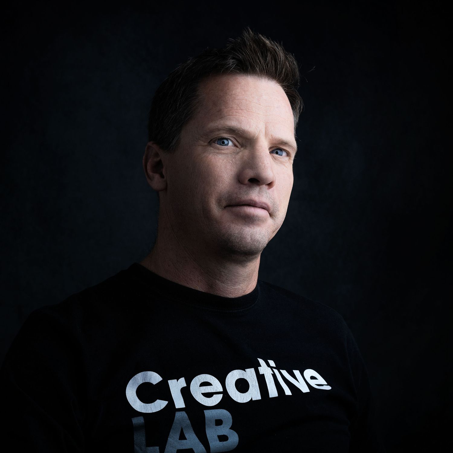 Professional portrait of a man in a Creative Lab black t-shirt against a dark studio background.