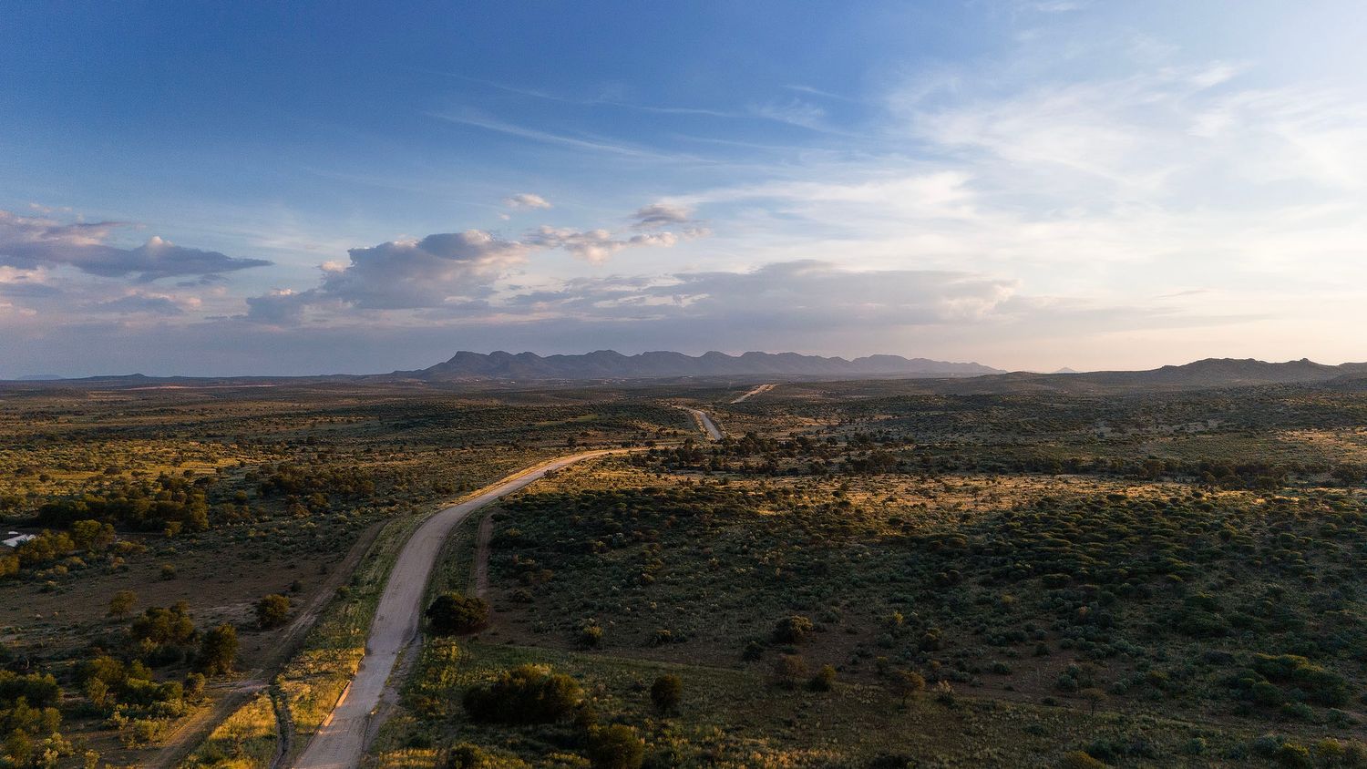Aerial panoramic view of a straight road through African savanna with distant mountain range.