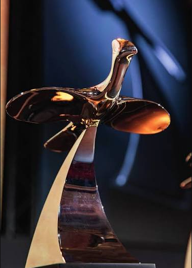 Shiny bronze bird-shaped award trophy on a golden base against a dark blue background.