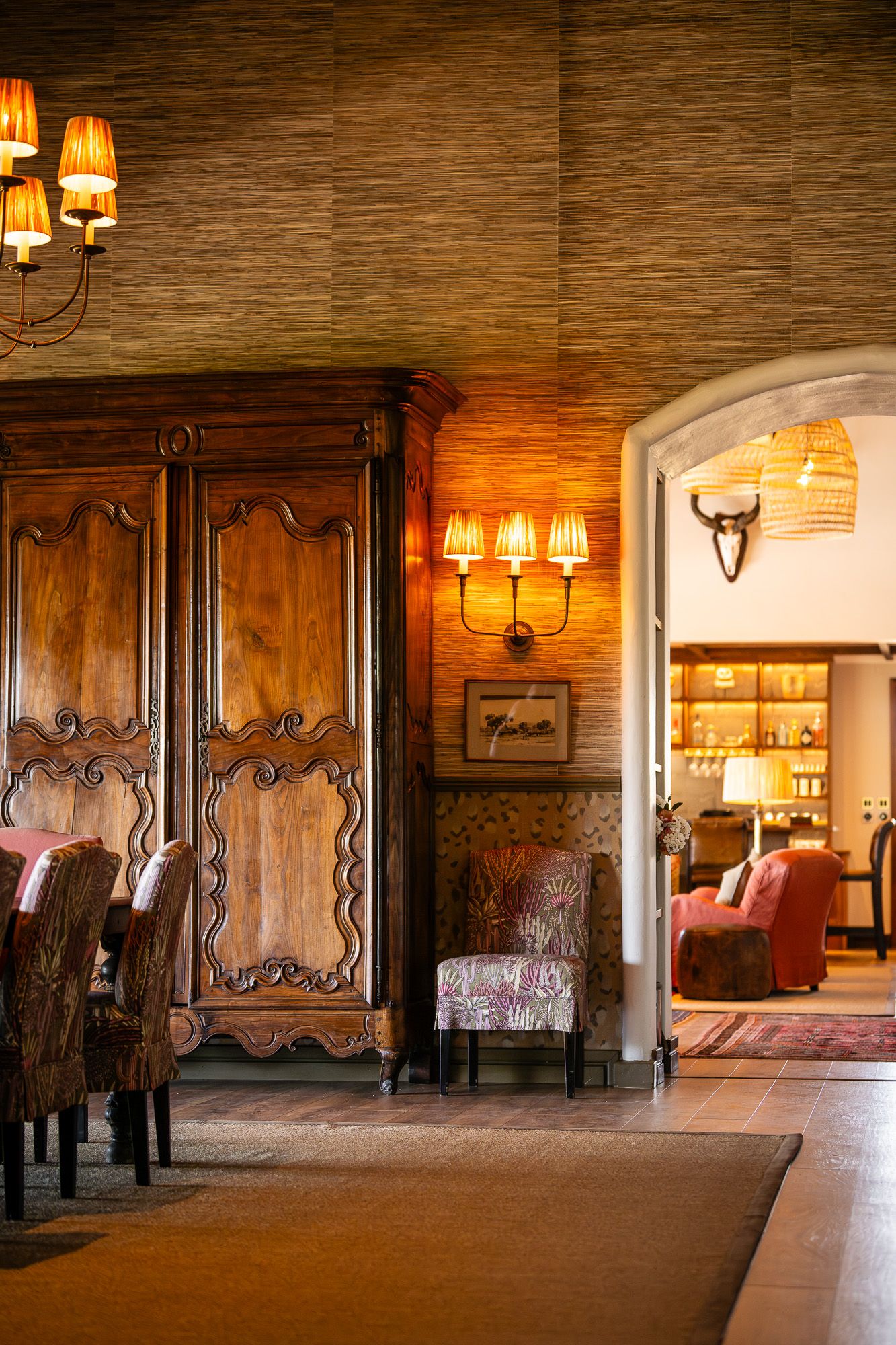 Elegant rustic interior with ornate wooden armoire, warm wall sconces, and arched doorway leading to a cozy lounge area.