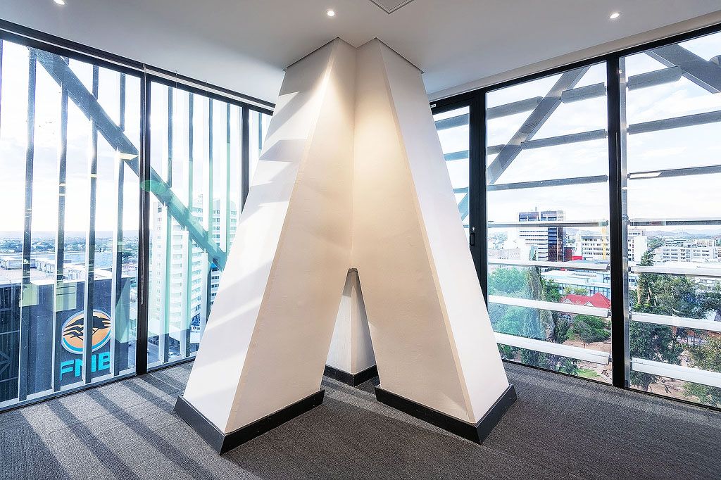 Large white geometric letter A sculpture displayed in modern office corner with panoramic city views.