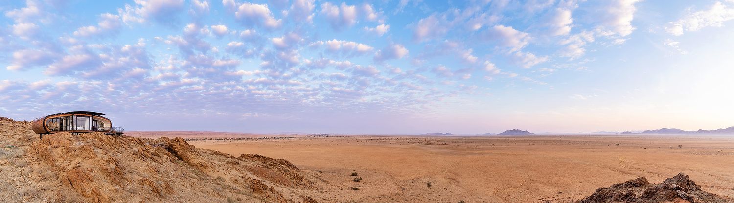Expansive panoramic view of an arid desert plain with distant mountains and dramatic cloud formations at sunset.