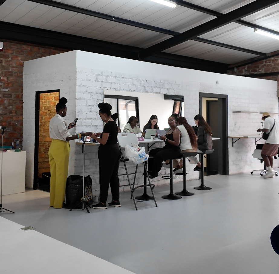 Women gathered at a modern salon studio with white brick walls, bar stools, and an open workspace in an industrial setting.