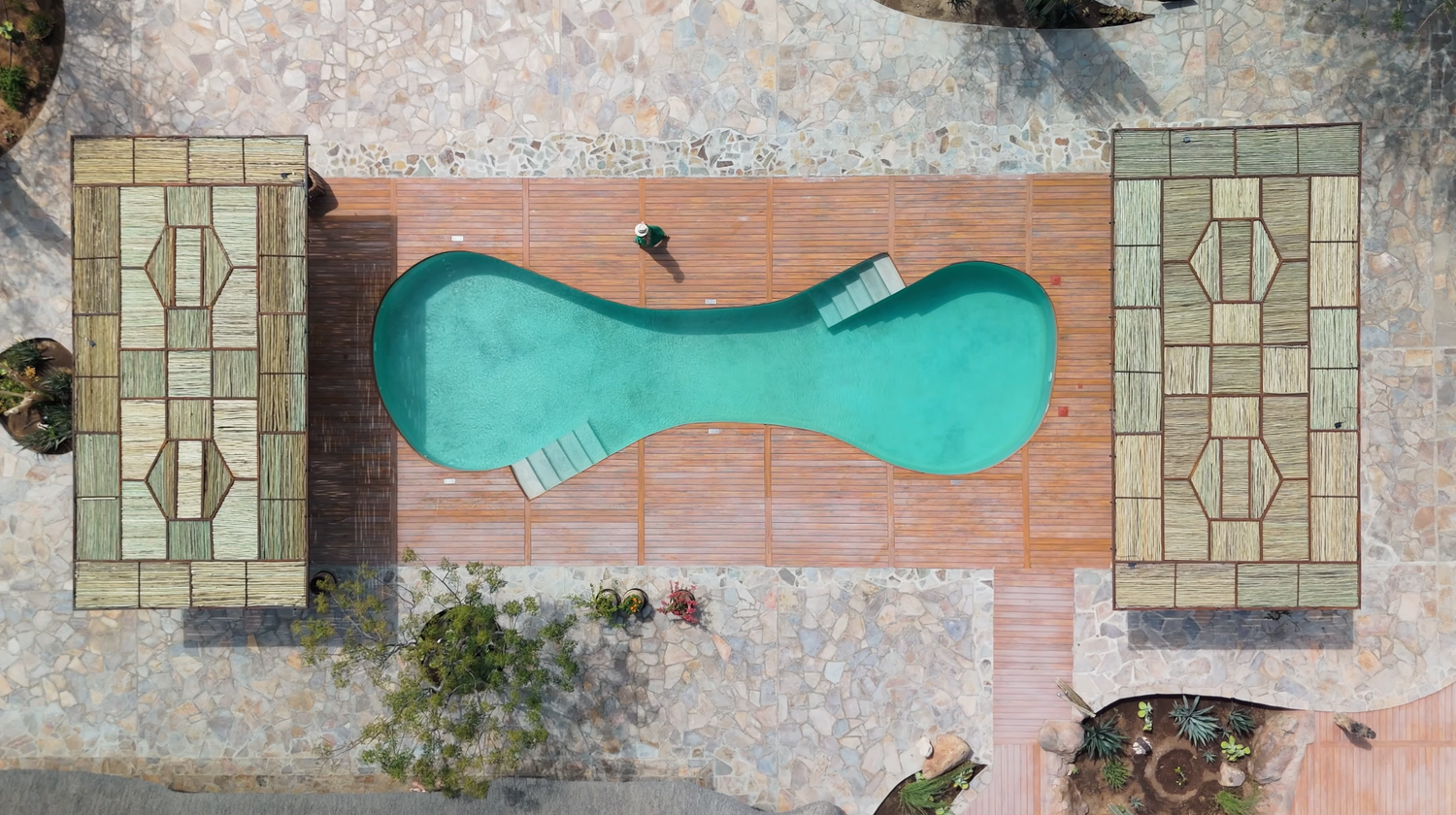 Aerial view of a unique kidney-shaped turquoise swimming pool surrounded by brick decking and stone patios.
