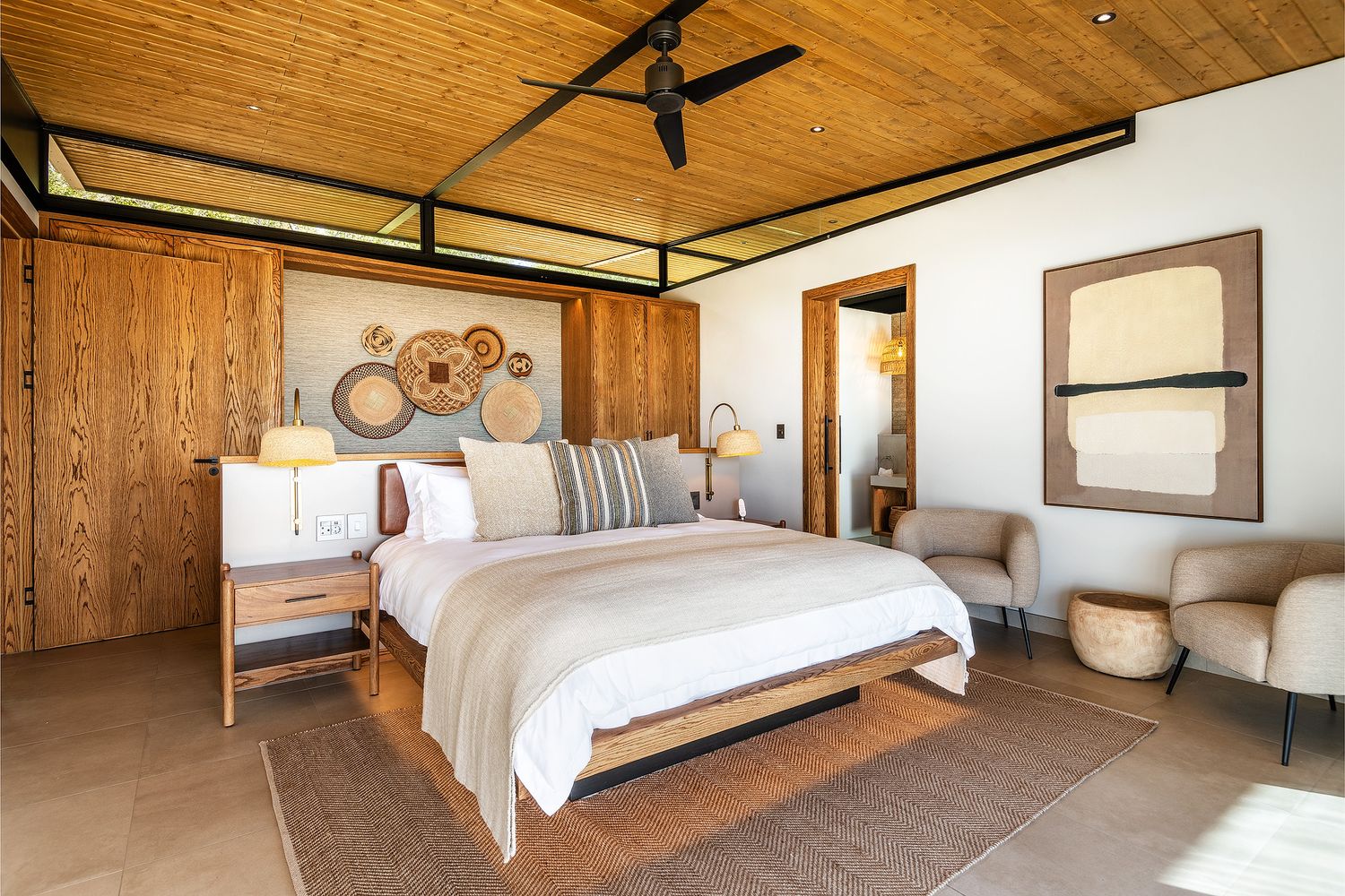 Elegant safari-style bedroom with wooden walls, king bed, ceiling fan, and neutral earthy tones.