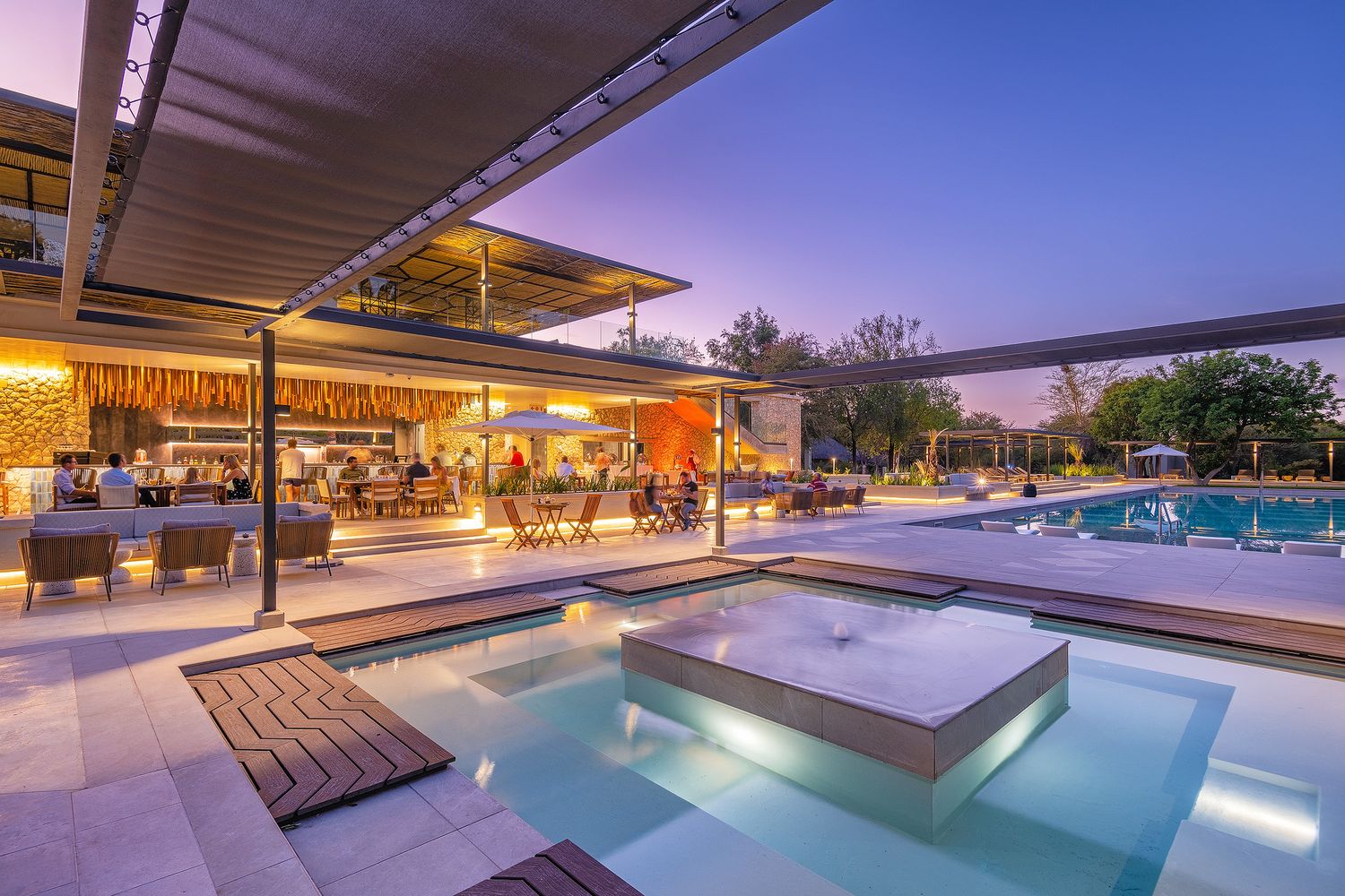 Luxury resort pool with glowing blue water, outdoor bar, and elegant seating area at dusk with purple sky.