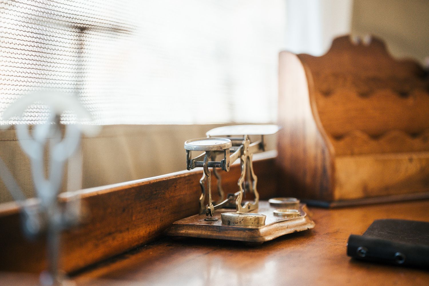 Vintage brass postal scale on antique wooden desk near window with letter holder and phone.