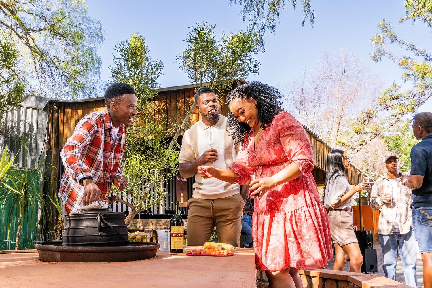Friends gather around a grill at an outdoor backyard barbecue party on a sunny day.