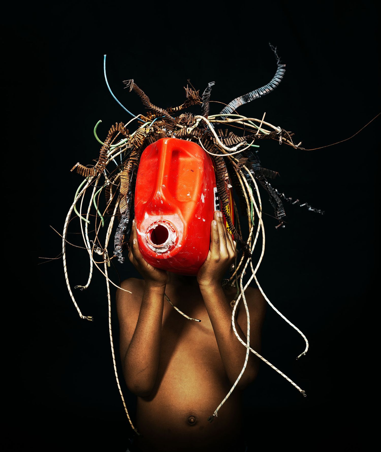 Person holding a red tribal mask adorned with twigs and roots against a dark background.