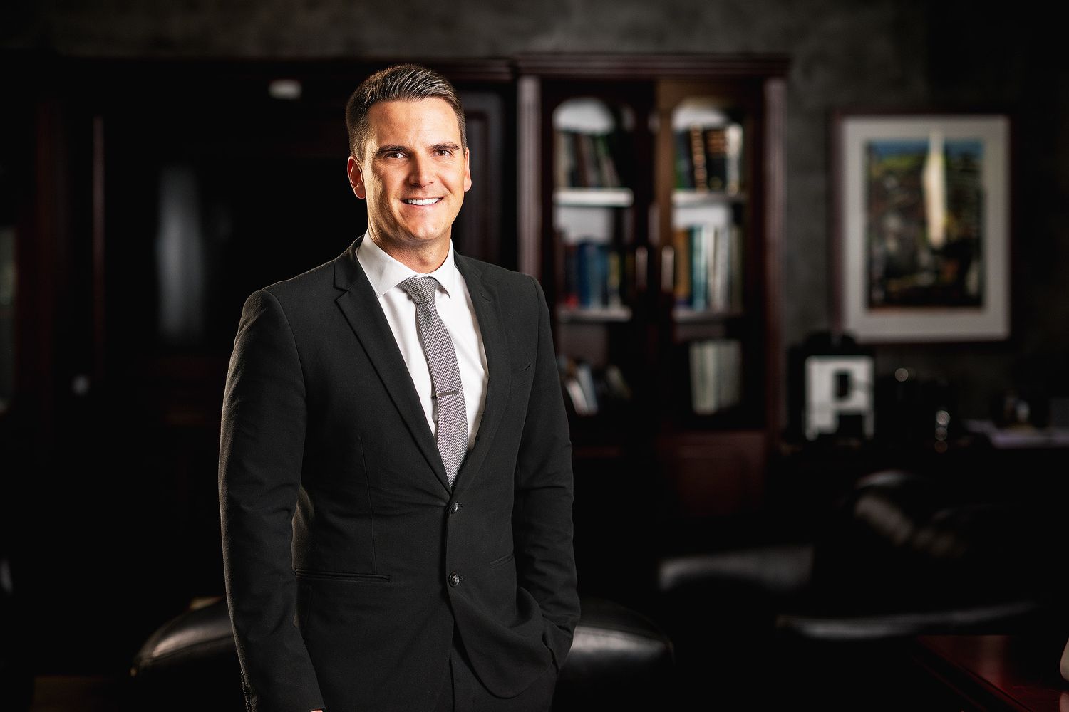Professional man in black suit and tie smiling confidently in a sophisticated office setting.