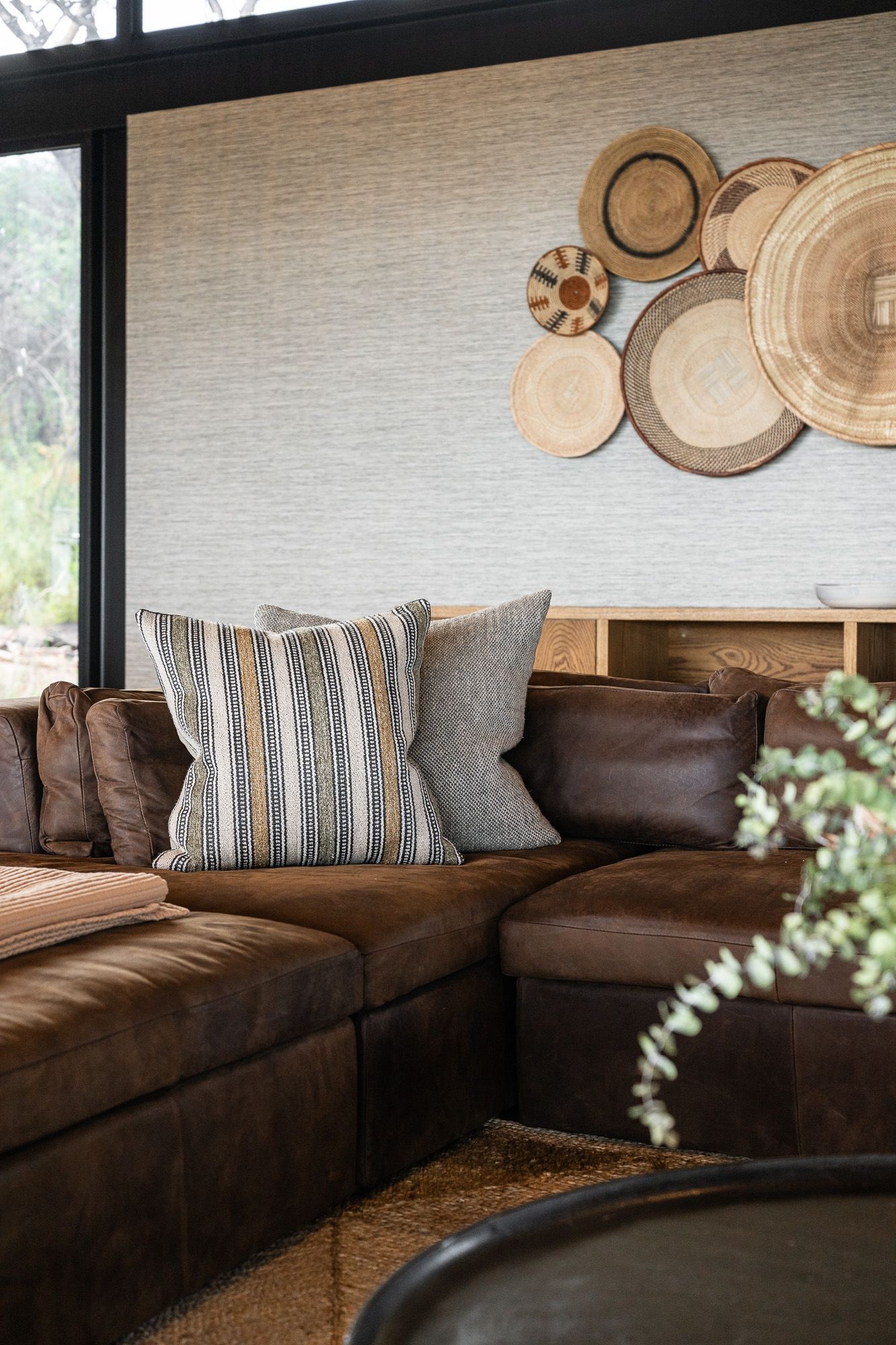 Brown leather sectional sofa with striped pillows and decorative wooden wall art in a safari-inspired lounge.