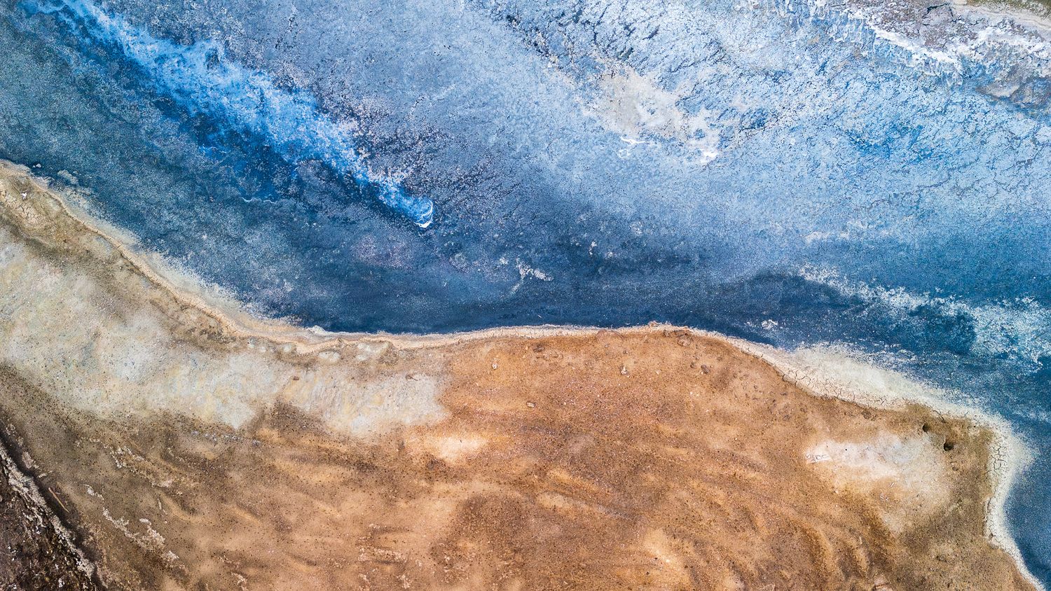 Aerial view of a stunning coastal landscape where turquoise ocean waves meet a sandy shoreline with salt flats.