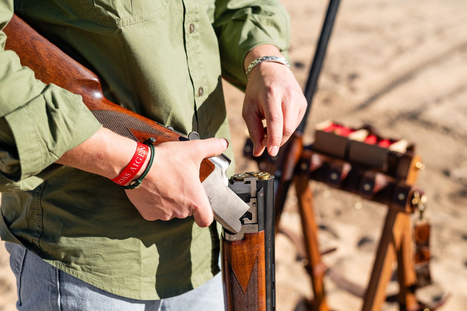 Person loading shotgun shells into a break-action shotgun outdoors at a clay shooting range.