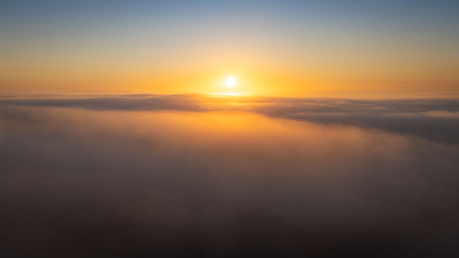 Aerial view of a stunning golden sunrise above a sea of clouds with warm orange and yellow hues filling the sky.