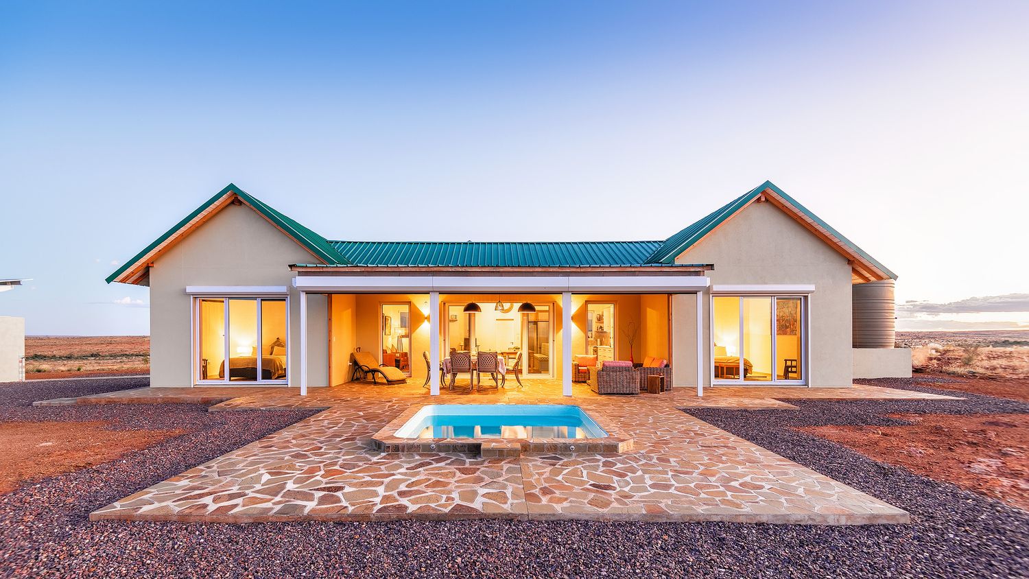 Luxury private villa with blue roof, stone patio, and small plunge pool at sunset in arid Namibian landscape.