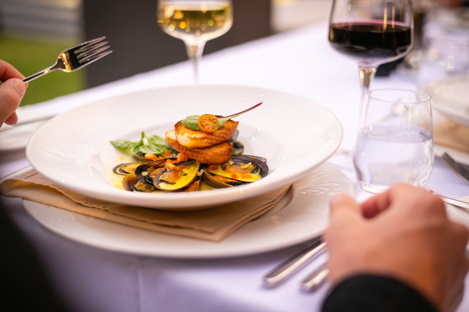 Elegant restaurant dish with grilled shrimp, mussels, and vegetables on a white plate, served with red and white wine.