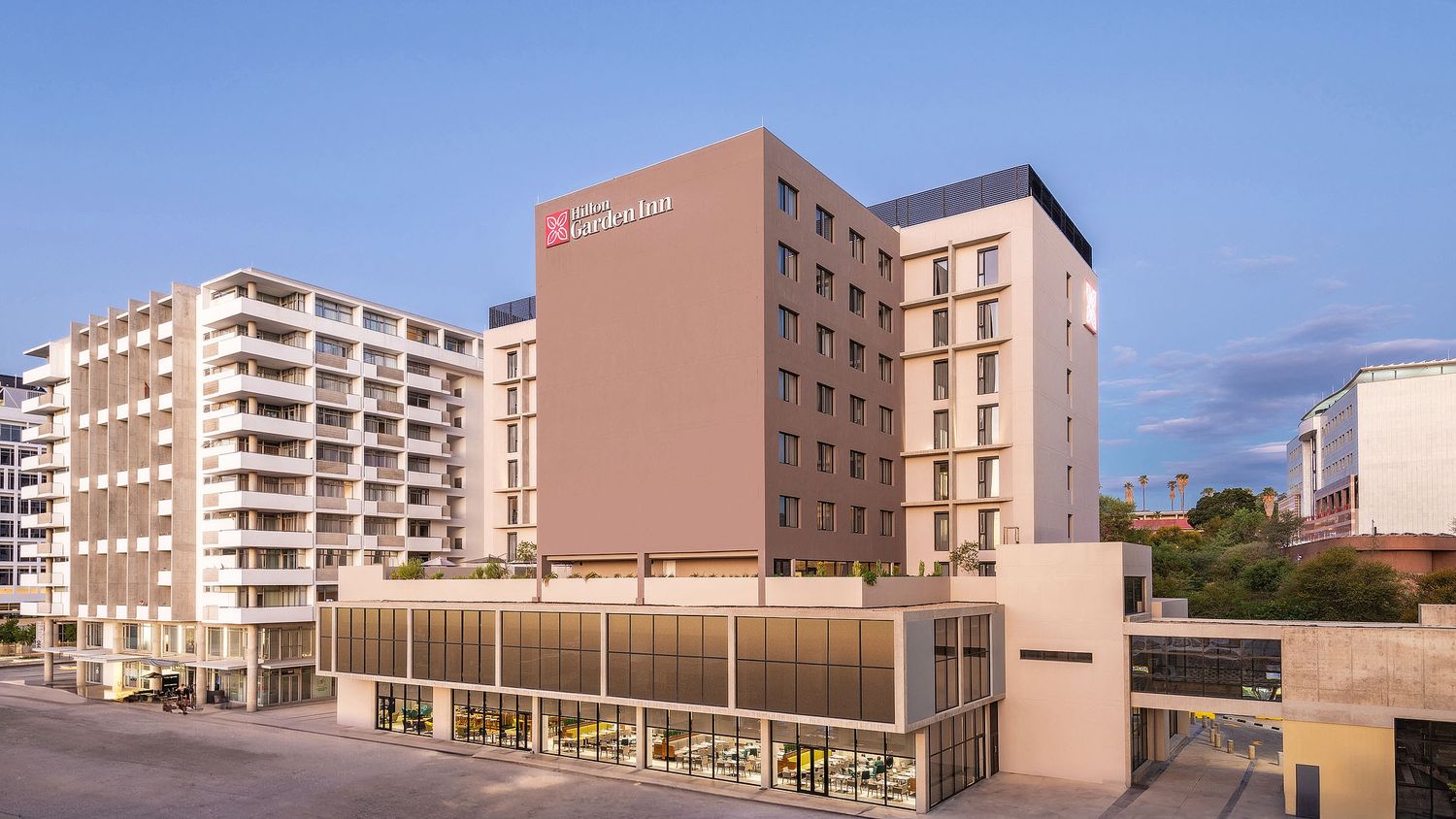 Modern Hilton hotel exterior with terracotta facade, multi-story glass windows, and urban surroundings at dusk.