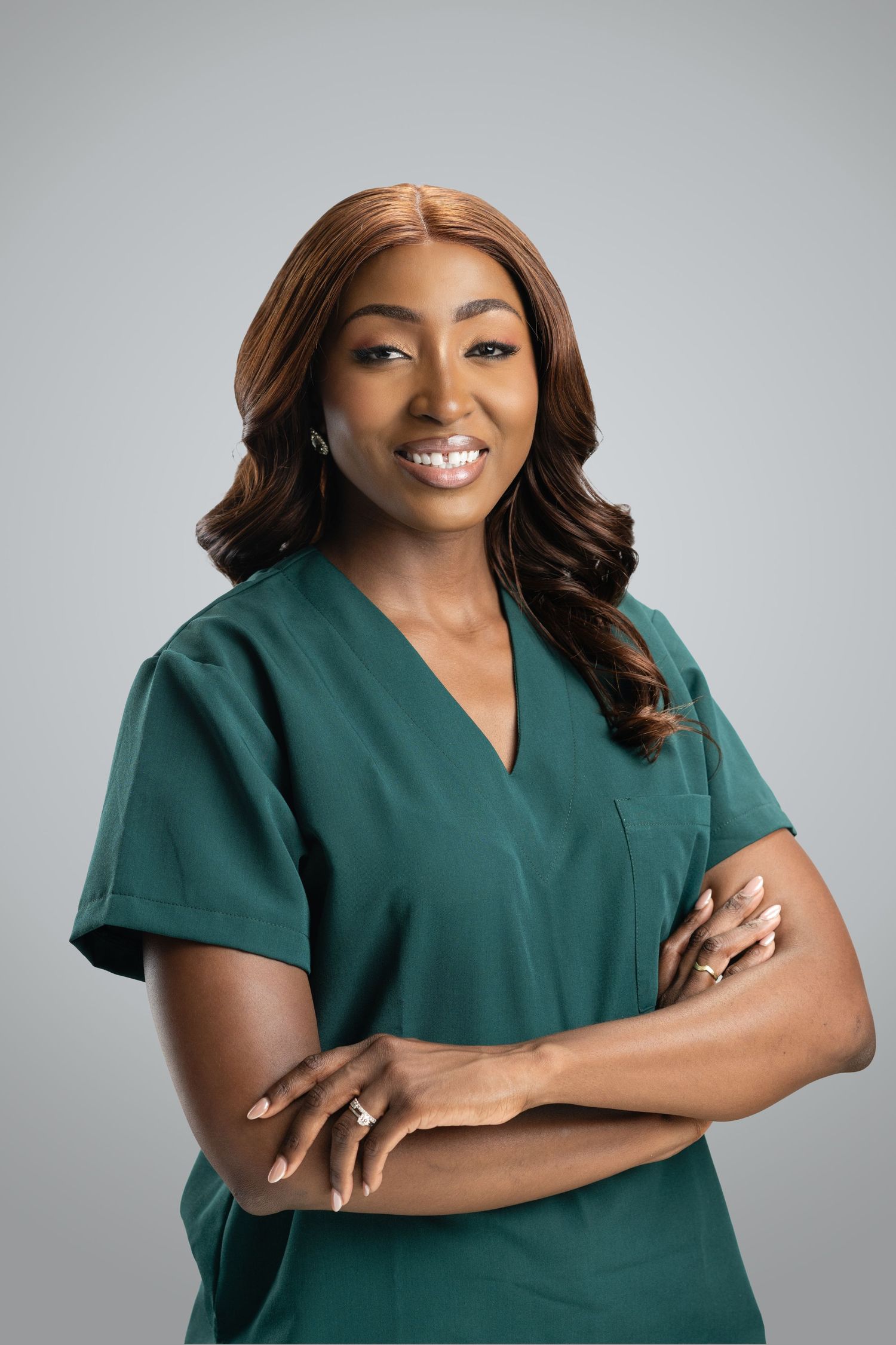 Smiling female healthcare professional in green scrubs with arms crossed against a gray background.