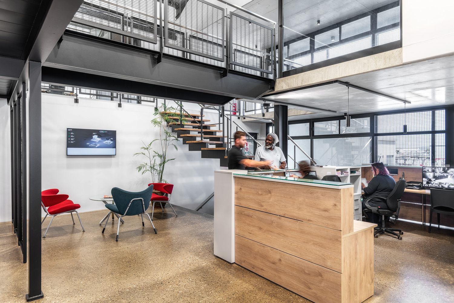 Modern industrial office with mezzanine level, wooden reception desk, colorful chairs, and open workspace area.