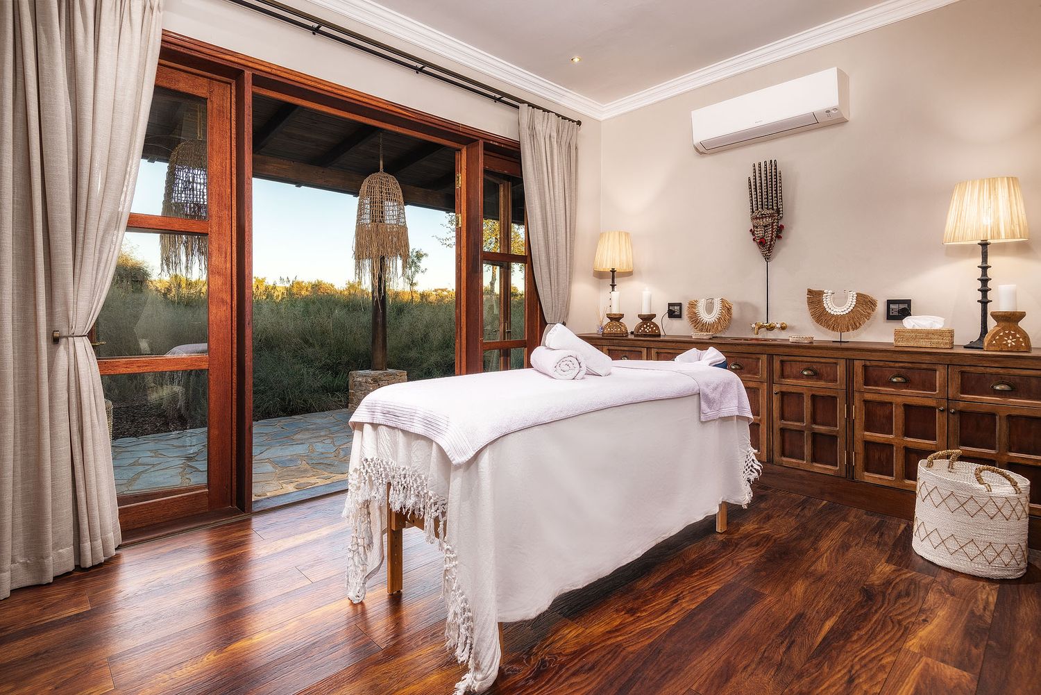 Luxurious spa treatment room with massage table, hardwood floors, French doors, and garden views.