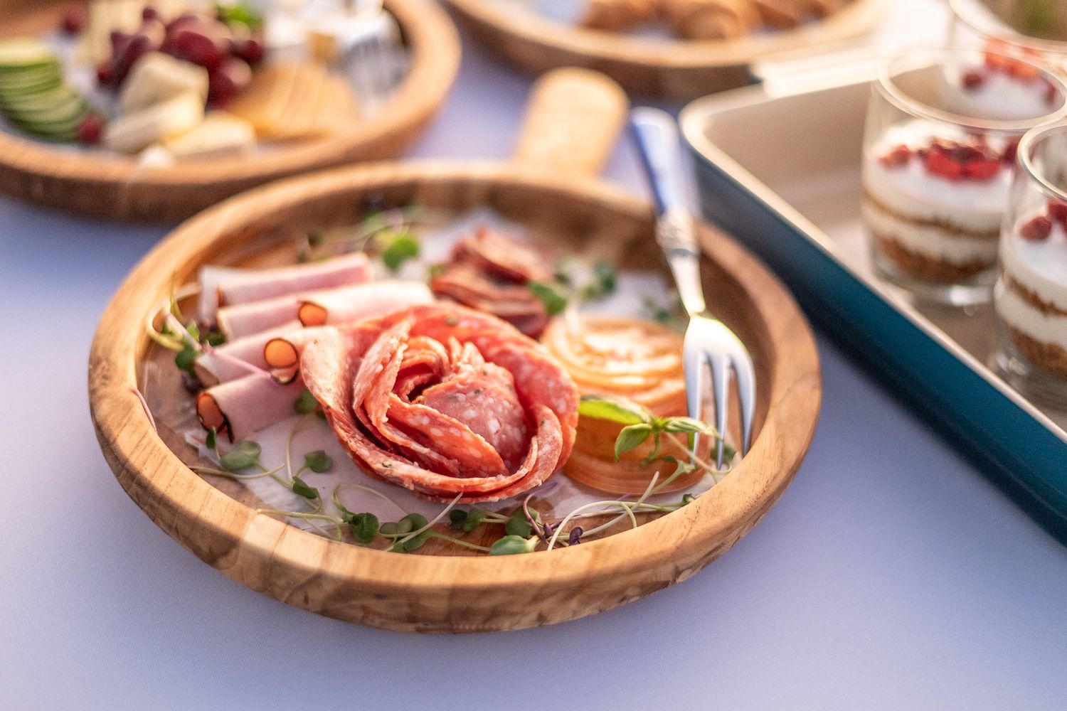 Elegant charcuterie board with salami rose, deli meats, and microgreens on a rustic wooden plate.